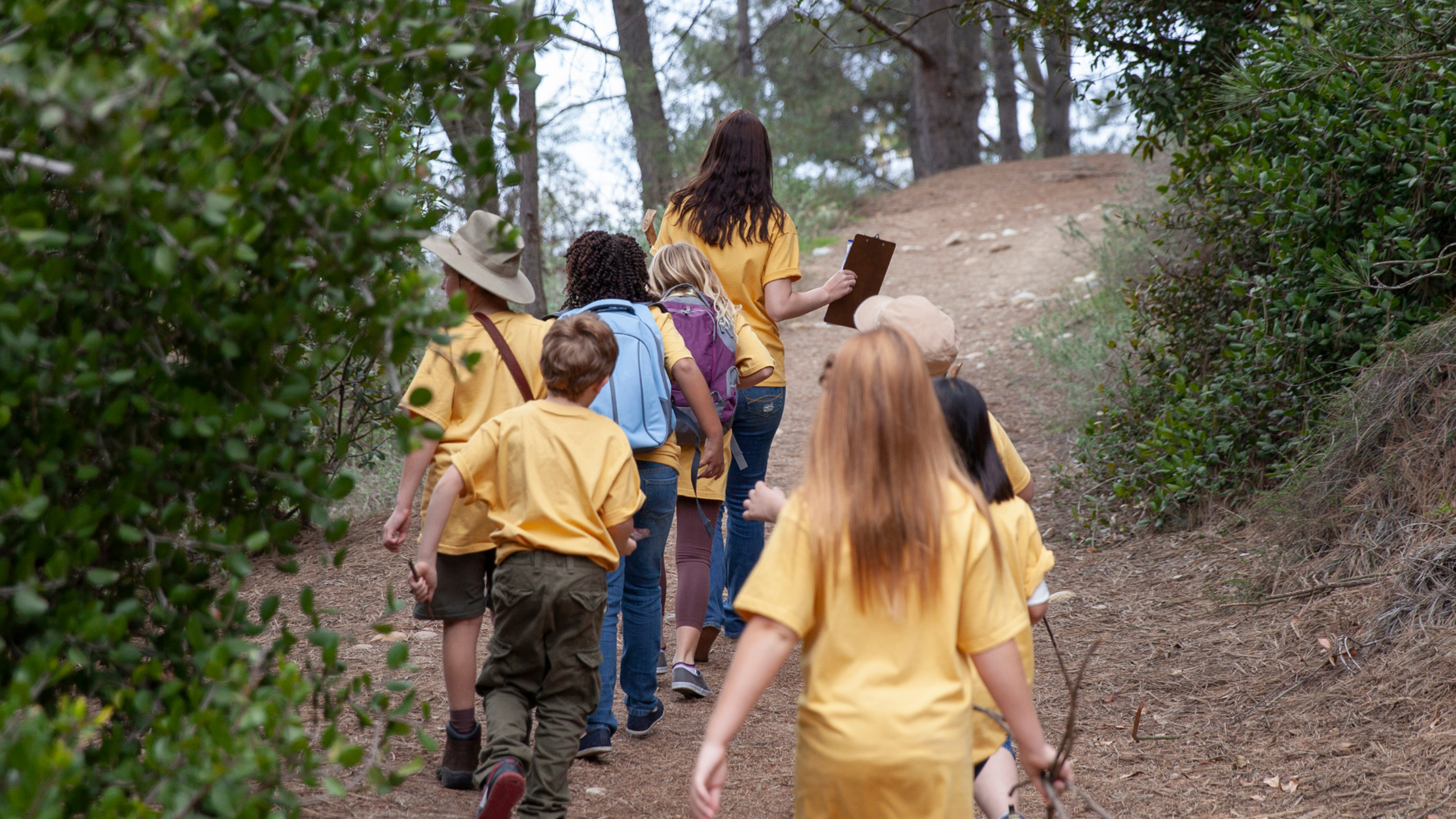 Image of group of children walking in the wood, followed by a leader