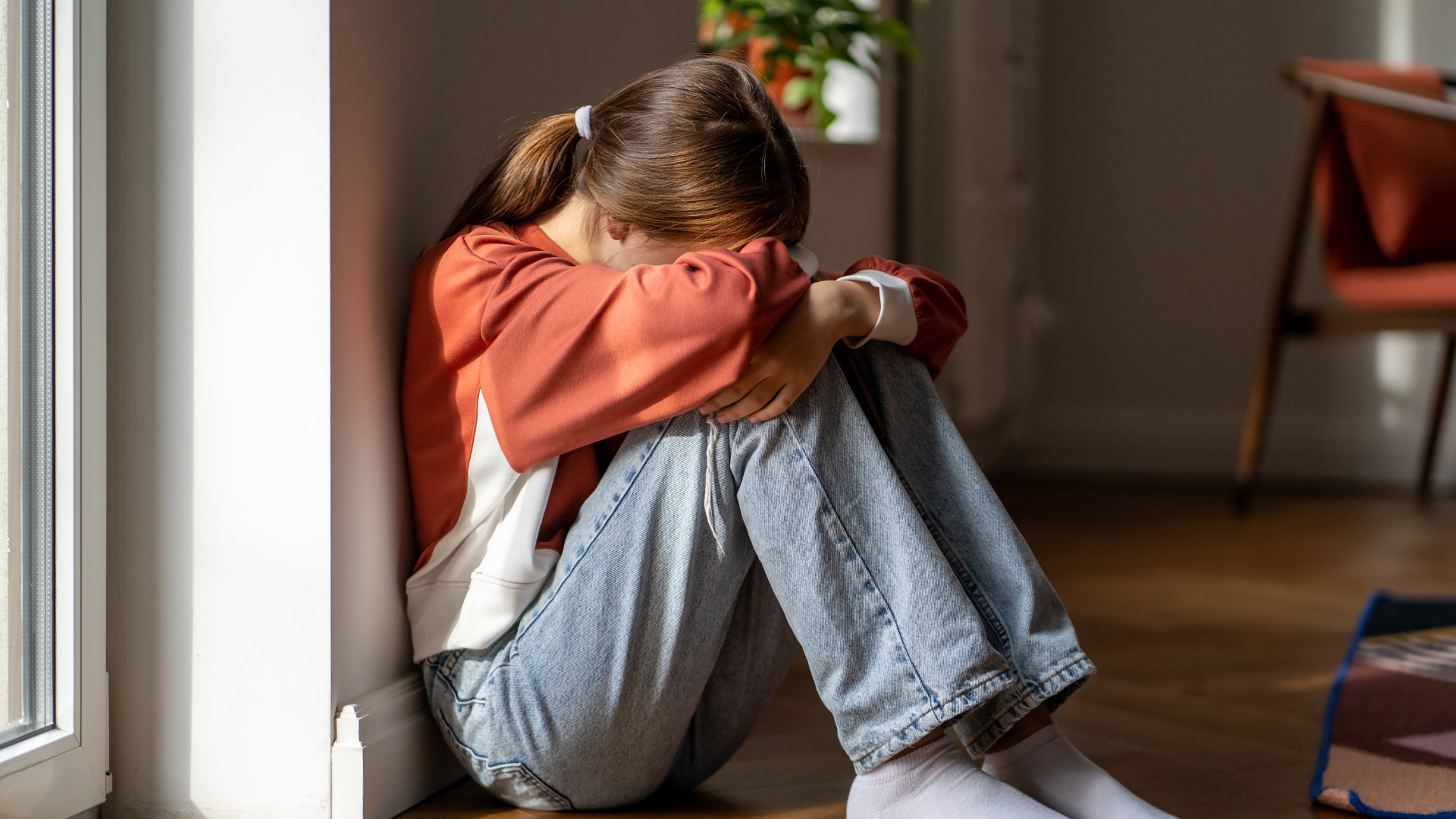 Image of young girl sitting on the ground with her face in her crossed arms