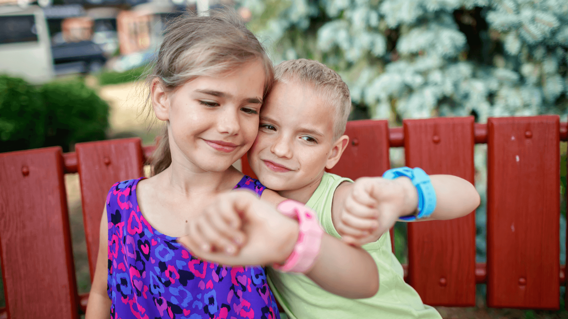Two kids looking at watches sitting on a bench