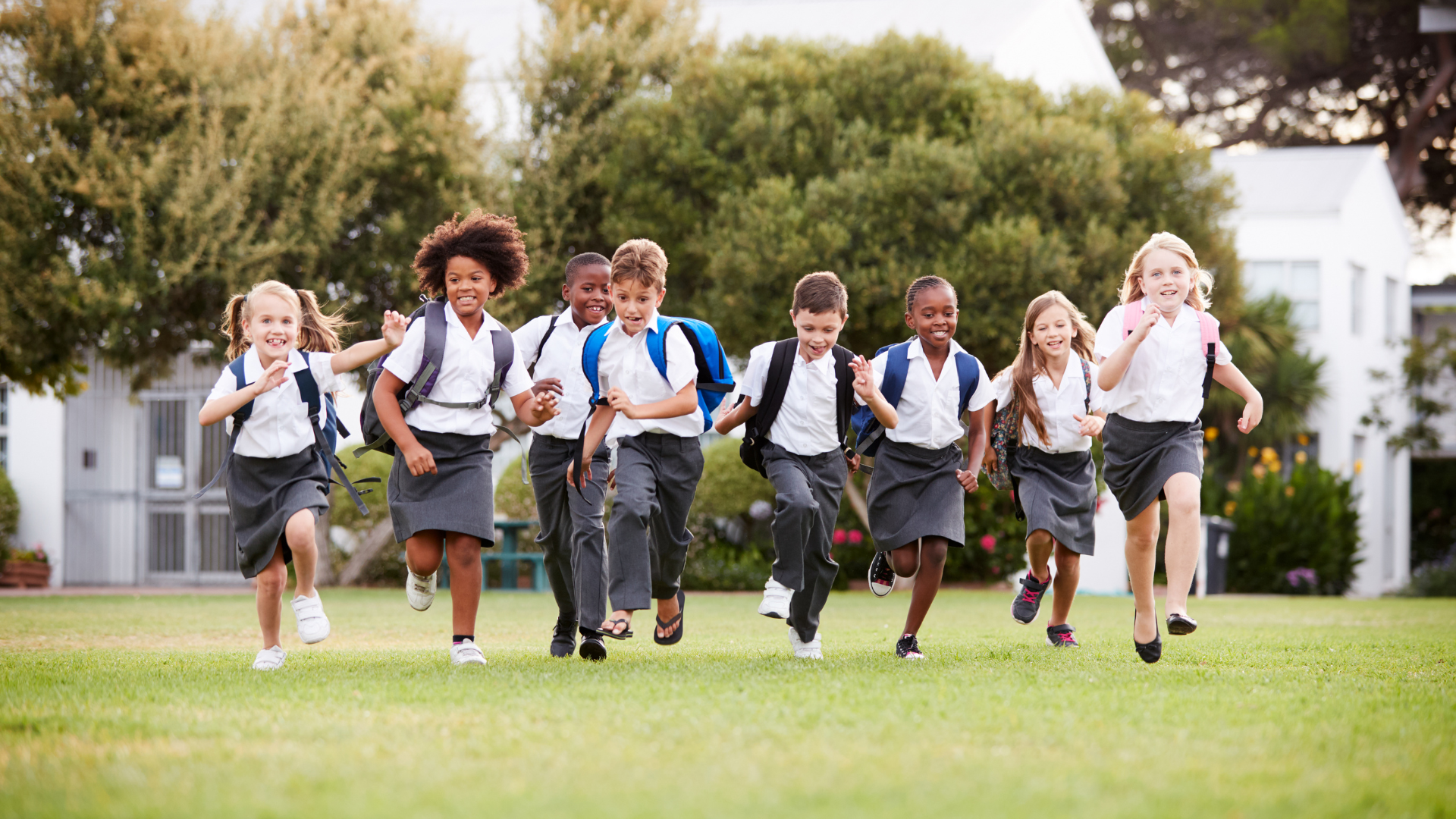 Eight children in school uniforms run on grass towards the camera